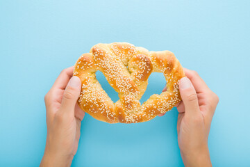 Young adult woman hands holding soft pretzel with sesame seeds on light blue table background....