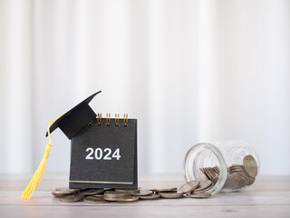 2024 desk calendar with graduation hat on stack of coins. The concept of saving money for...
