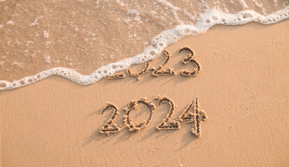 Handwritten inscription 2023 and 2024 on the beach in the sunset time. The concept of Goodbye 2023...