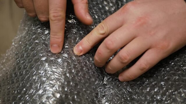 Fingers popping bubbles in bubble wrap close-up anti-stress therapy. Nervous man press plastic bubble wrap as a stress relief. man close up pressing bubble wrap with fingers from delivery packaging.