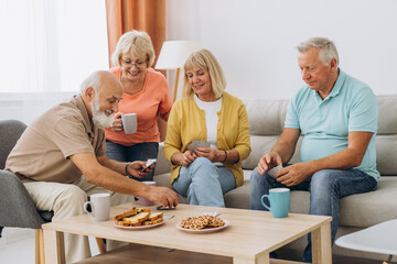 Group of senior people laughing while relaxing at home and playing cards.