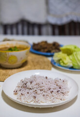 The cooked brown rice on the white plate with Thai food