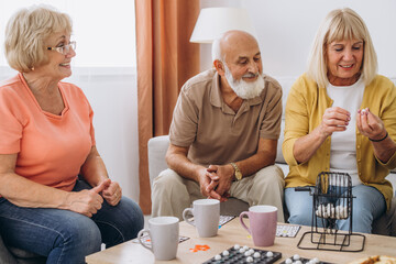 Group of four cheerful senior people playing bingo game in nursing home