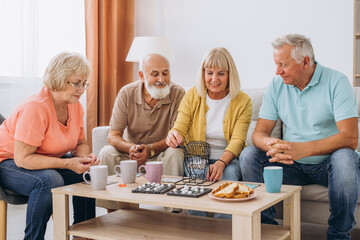 Group of four cheerful senior people playing bingo game in nursing home