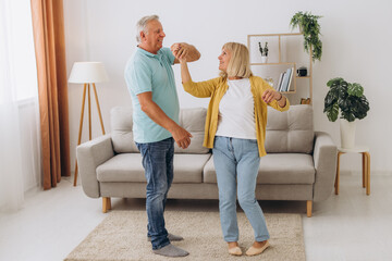 Happy senior couple dancing to music together in living room