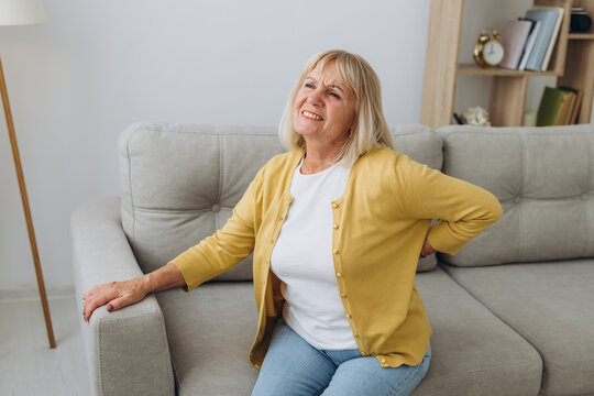 Senior woman having backache and touching her back in living room at home