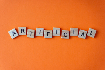 Obraz premium Word artificial. The phrase is laid out in wooden letters top view. Orange flat lay background