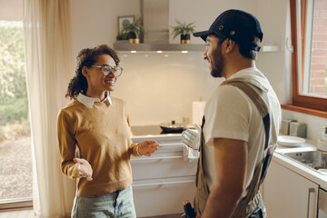 Beautiful young woman talking to male handyman while standing at the kitchen at home