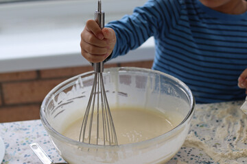 Child making waffle with the waffle machine plate. Child holding whisk mixing  wet cake mixed...