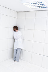 Young frustrated girl in a straitjacket is in an isolated white room in a mental hospital	