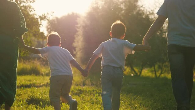 Large family of parents and children runs joining hands across meadow. Huge family spends time actively running on grass on holiday. Little brothers and parents run together in field under sunlight