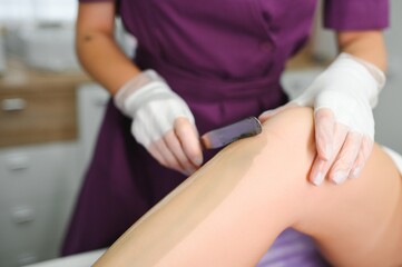 A master applies depilatory wax to a young woman's leg for hair removal. Depilation with wax....