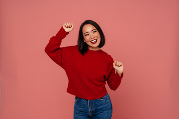 Smiling asian woman dancing isolated over pink studio background
