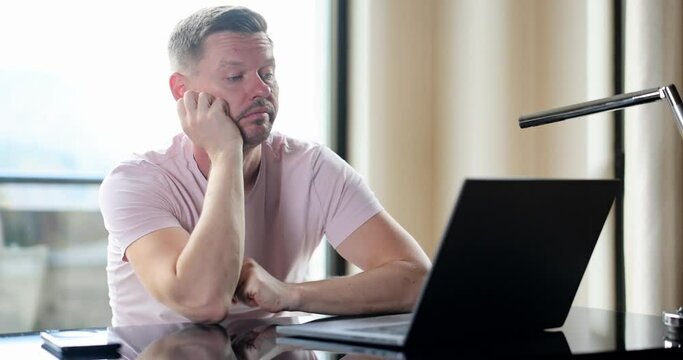 Boring man and stupid work man looks at laptop. Silly business tasks freelancer looking at laptop with dumb emotions sitting at table