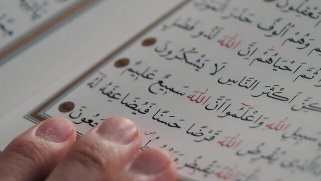 Close-up of a page from the Quran. The reader places his hand on the page.
