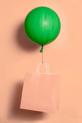 Big green ballon holding paper bag for delivery on peach fuzz color background. High quality photo