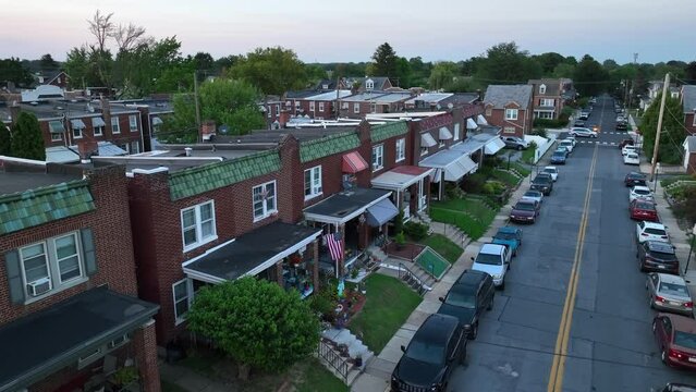 Row houses with awnings on a tree-lined residential city street. Aerial view of neighborhood in urban USA. Rising shot with American flag during sunset.