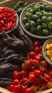 Different types of chilies. Brazilian Biquinho Yellow, Brazilian Red Olive, Peruvian Machu Picchu, and tabasco on a plate. Table spin. Vertical video.