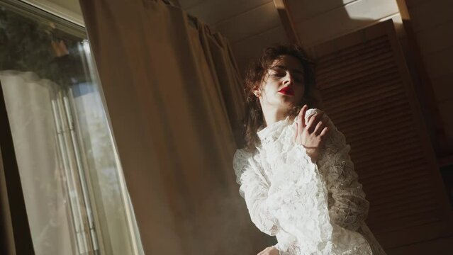 A fashion model in a wedding dress poses in a room with smoke and sunlight. Concept for fashion wedding photography