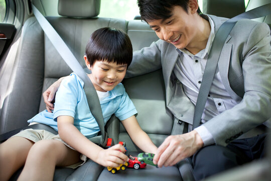 Cheerful father and son playing toy cars in back seat