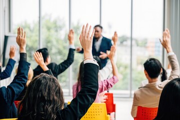 Business professionals come together for a corporate event featuring a conference and convention. Raised hands demonstrate active involvement in a meeting training seminar and discussions.