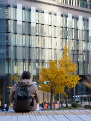 秋の名古屋駅前の高層ビル群と休憩している一人の男性観光客の姿