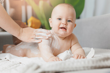 Mother applying body cream on her little happy baby son at home. Concept lotion for skin of infant