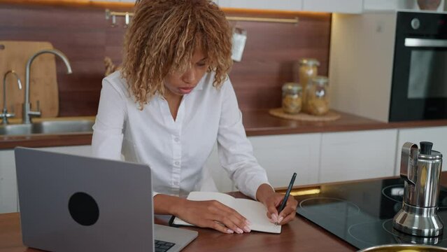 blond woman journaling or planning day handwriting in notebook in the kitchen freelancer at workplace