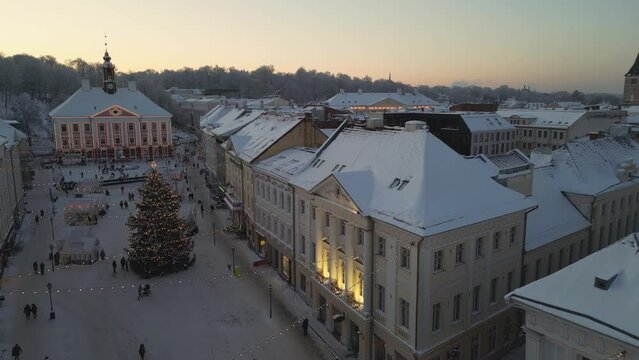Tartu, Estonia, the enchanting Christmas market beckons during the evening's embrace. Illuminated by a myriad of twinkling lights, a resplendent Christmas tree stands tall, adorned with tree lights.