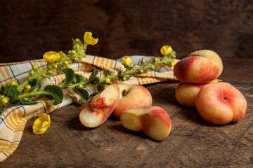 Half and several whole saturn peaches or flat peaches on wooden background with yellow kitchen...