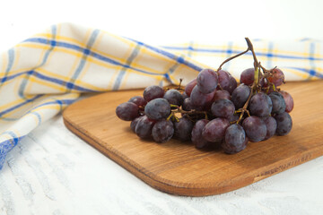 Cutting board with bunch of organic black grapes on white wooden background..