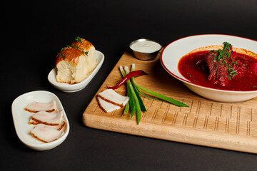 traditional Ukrainian borsch near garlic buns, pork lard and green onions on cutting board on black