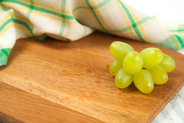 Cutting board with bunch of organic green grapes on white wooden background..