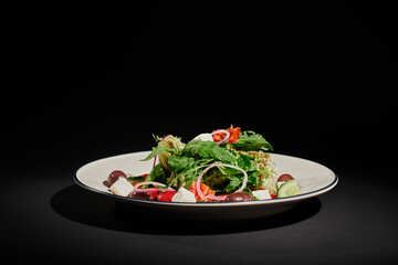healthy eating, delicious Greek salad with feta cheese, red onion, arugula leaves on black backdrop