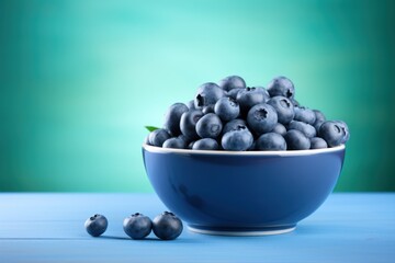  a blue bowl filled with blueberries sitting on top of a table next to three blueberries on top of a blue table.