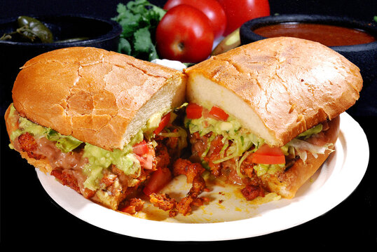 Torta Mexicana de adobada con guacamole lechuga y tomate con fondo de tomates y cilantro
