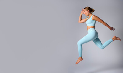Fototapeta na wymiar Studio Shot Of Woman Wearing Gym Fitness Clothing In Mid-Air Exercising On Grey Background