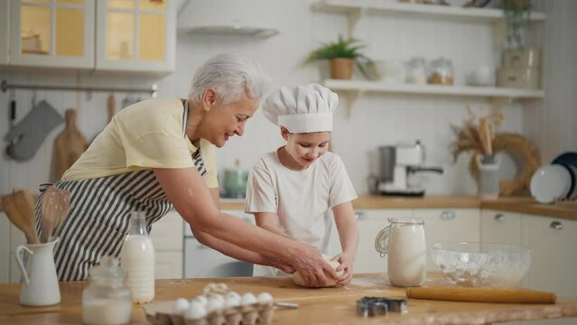Happy family, granny and granddaughter cook together in kitchen. They make cookies star shape from dough. Homemade bakery, sweets, pastry concept. Smiling pre-teen girl wears cook's cap helps grandma.