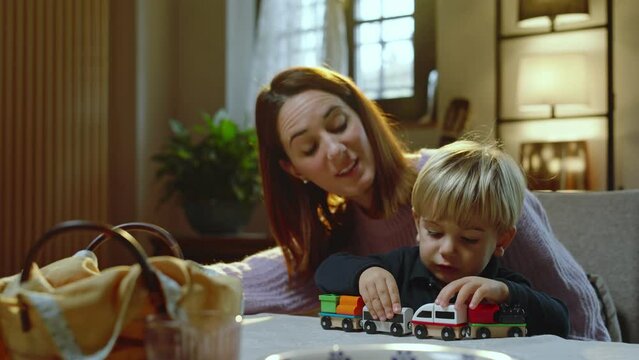 To entertain her son at the table, a young mother lets him play with a wooden train.
The mother and the child play and are happy