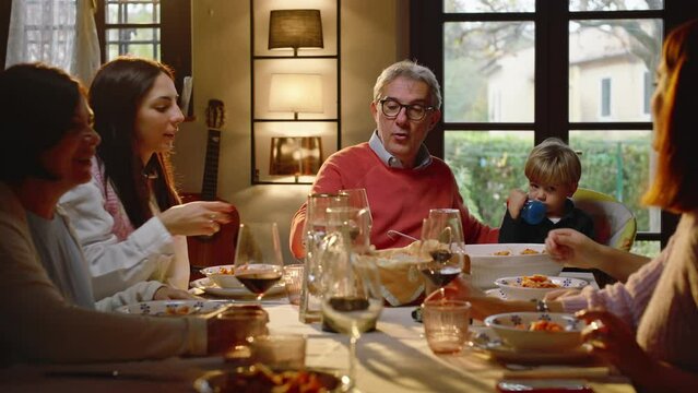 A family sitting at the dining table, talking, laughing and making a toast with glasses of wine.
Concept of family, tradition and love