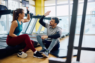 Happy couple giving high five after exercising in a gym.
