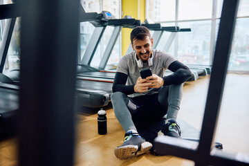 Happy athlete using cell phone while taking break from exercising in gym.