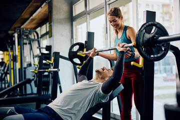Happy athletic couple exercising with barbel in gym. - obrazy, fototapety, plakaty