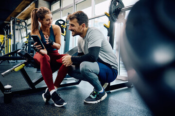 Happy athletic couple using app on smart phone during sports training in gym.