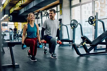 Foto op Plexiglas Happy athletic couple exercising with hand weights in lunge position in gym. © Drazen