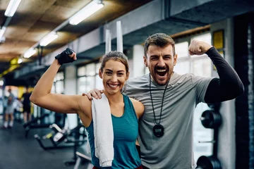 Foto op Plexiglas Happy athletic woman and her fitness instructor flexing muscles in gym while looking at camera. © Drazen