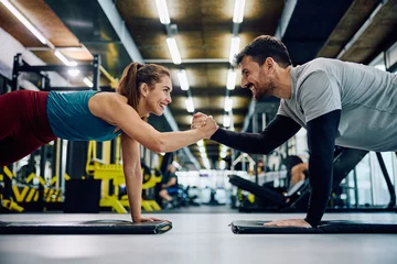 Foto op Canvas Happy athletic couple cooperating while exercising in plank pose in gym. © Drazen