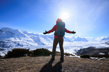 Woman hiker enjoy the view on mountain top cliff edge face to glacier mountains