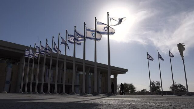 Orthodox Jewish men walk towards the Knesset (legislative branch of the Israeli government), in between waving national flags
