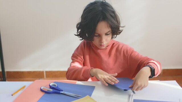 A child makes a creative toy from colored paper at the table. boy makes a snowflake from blue paper. children's creativity.